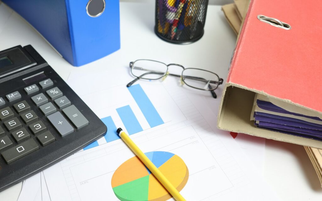 Schreibtisch mit Taschenrechner, Diagrammen und Ordnern zur Analyse von Deckungsbeitrag und Fixkosten