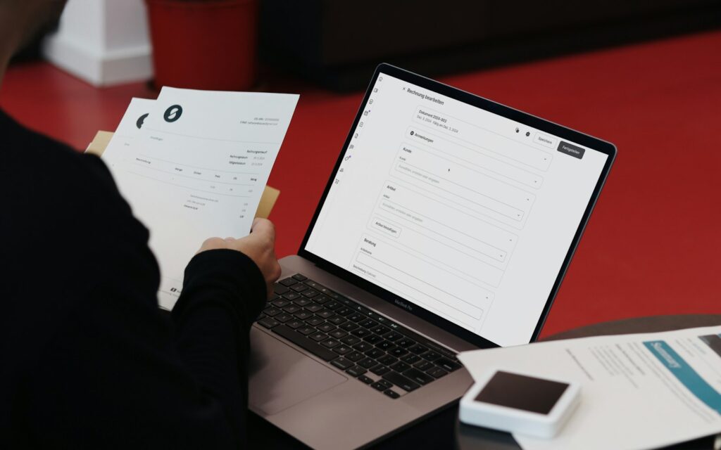 Selbstständige prüft am Schreibtisch mit Laptop und Unterlagen, wie sie eine E-Rechnung empfangen kann
