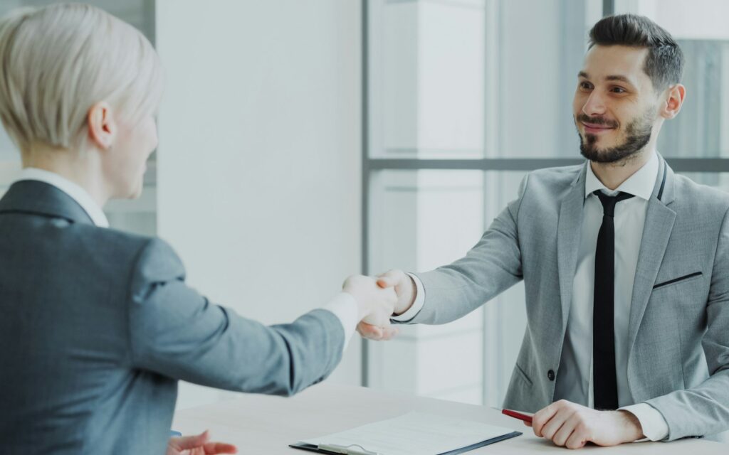 Zwei Geschäftsleute reichen sich über einen Tisch die Hand – Empfehlungsmarketing schafft Vertrauen