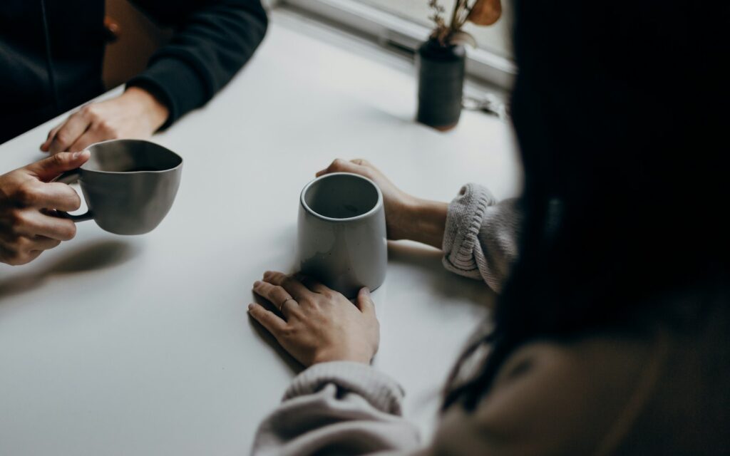 Zwei Personen mit Kaffeetassen im Gespräch am Tisch als Symbol für Empfehlungsmarketing