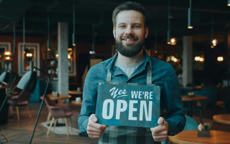 Inhaber hält ein Open-Schild im Restaurant – wer ein Gewerbe anmelden will, startet mit der Anzeige beim Amt