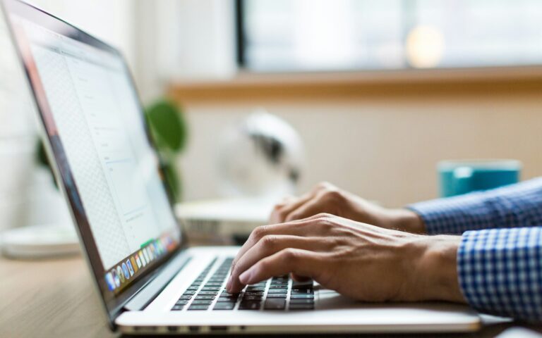 Person tippt auf einem silbernen Laptop und plant die Google Ads Kosten einer Kampagne