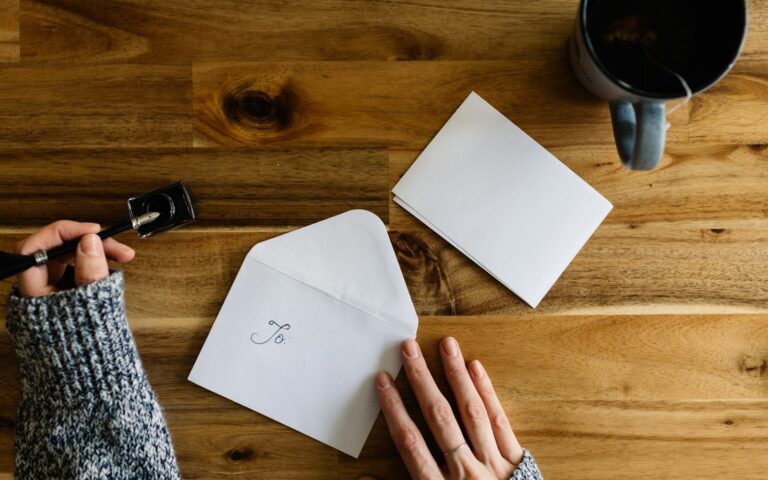 Person schreibt neben einer Kaffeetasse auf ein Blatt Papier: Mahnung schreiben an einen säumigen Kunden