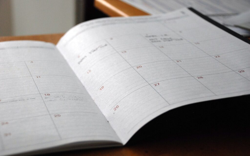 Aufgeschlagener Monatsplaner auf einem Holztisch für den Marketingplan und Maßnahmenkalender