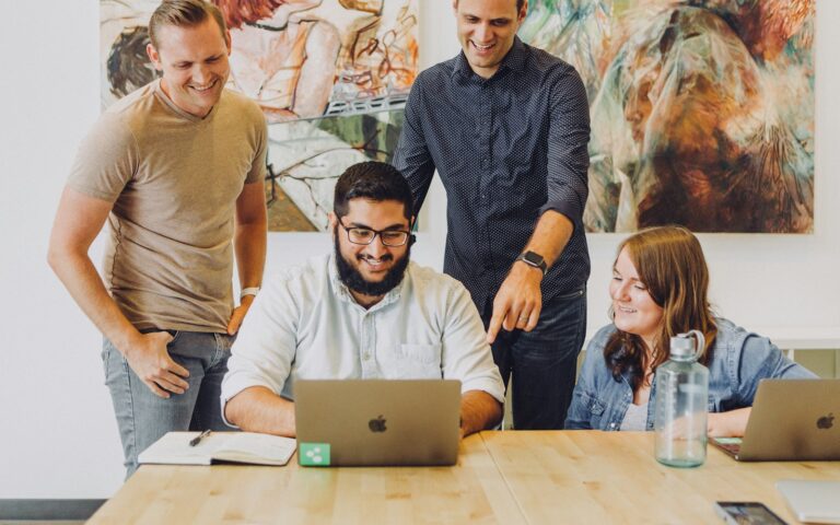 Vier Kollegen lachen gemeinsam am Laptop, Symbolbild für Mitarbeiterbindung im Team
