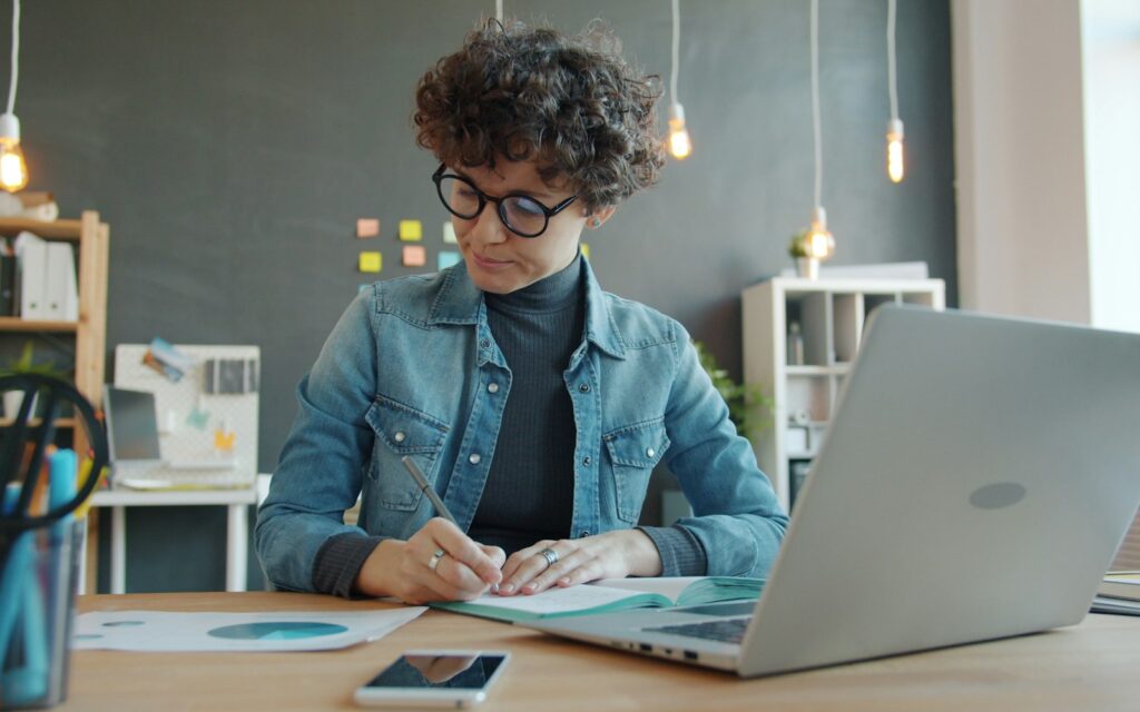 Unternehmerin notiert am Schreibtisch die Pflichtangaben, um eine Rechnung schreiben zu können