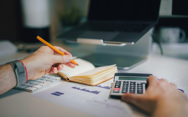 Unternehmer prüft am Schreibtisch mit Taschenrechner und Notizbuch die Rücklagen für seinen Betrieb