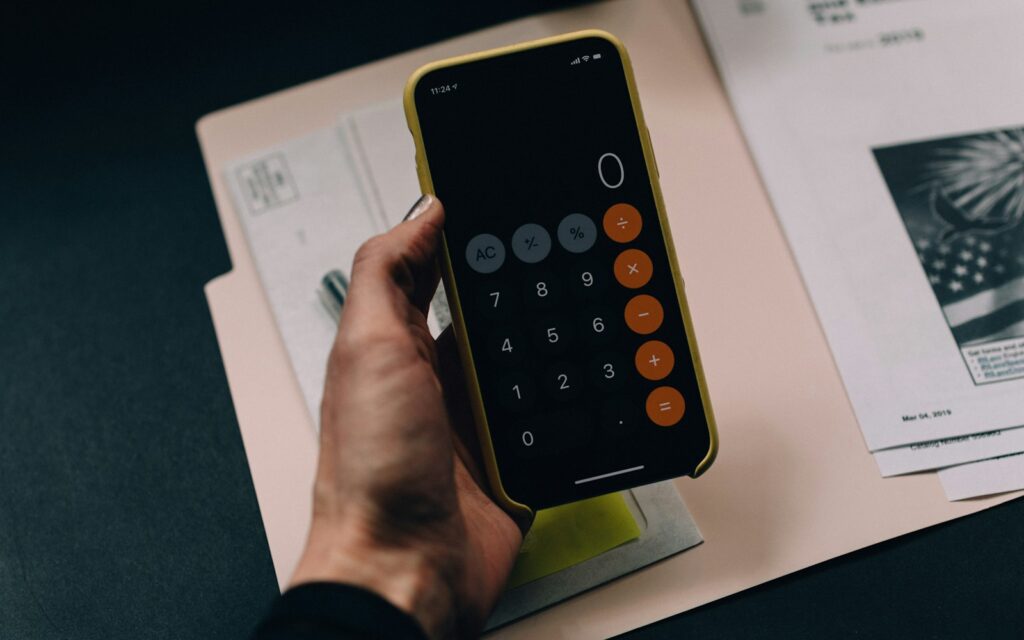Hand mit Smartphone-Taschenrechner über einer Mappe beim Berechnen von Skonto