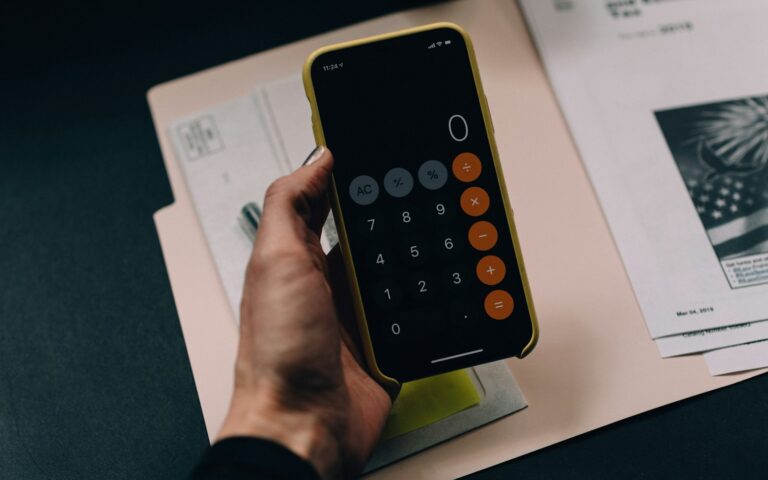 Hand mit Smartphone-Taschenrechner über einer Mappe beim Berechnen von Skonto