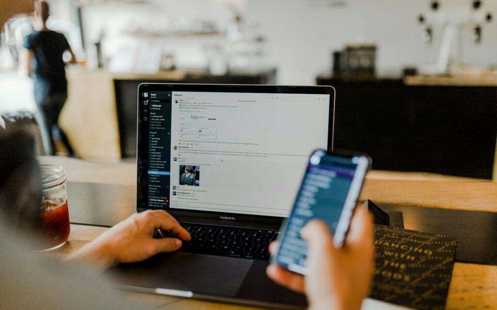 Person mit Smartphone und Laptop plant B2B-Social-Media-Beiträge für ihr Unternehmen